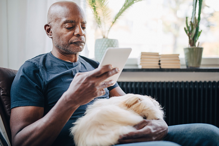 Man with a dog on his lap reading e-reader